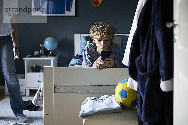 Junge benutzt Mobiltelefon  während er zu Hause auf dem Bett liegt