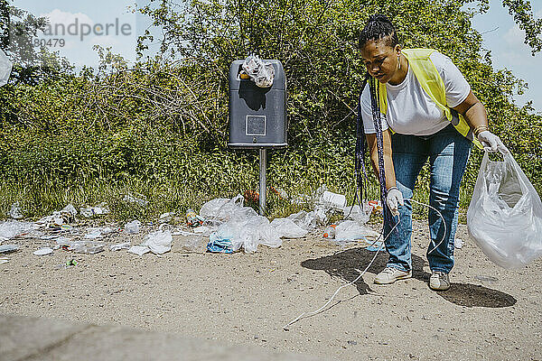Ältere Umweltschützerin  die an einem sonnigen Tag im Park Müll aufsammelt