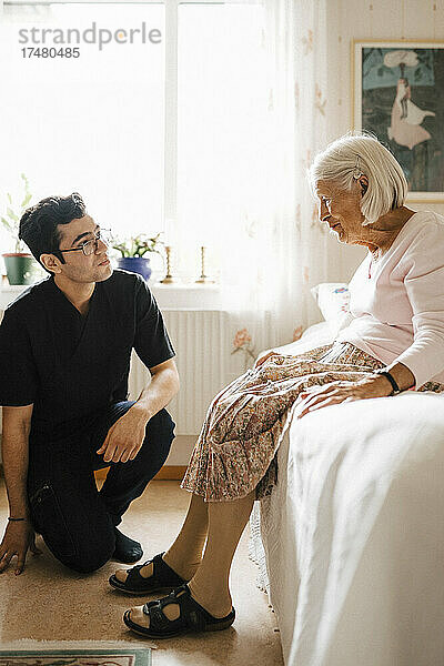 Ältere Frau im Gespräch mit einem jungen Mann aus dem Gesundheitswesen im Schlafzimmer zu Hause