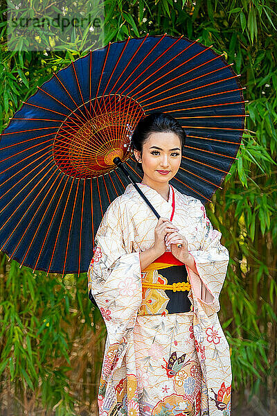 Porträt einer lächelnden Frau im Kimono und mit Sonnenschirm im Park
