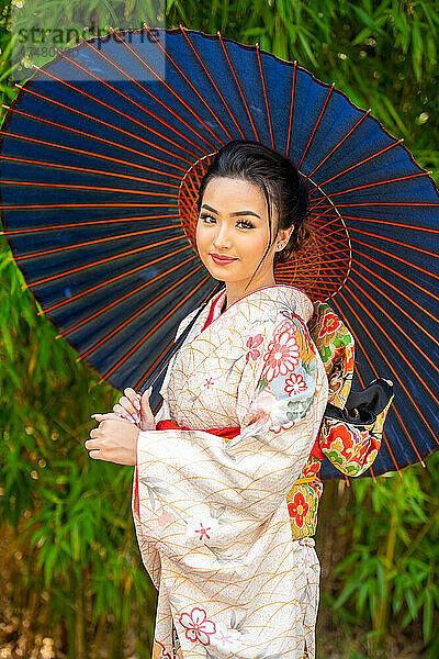 Porträt einer lächelnden Frau im Kimono und mit Sonnenschirm in der Hand