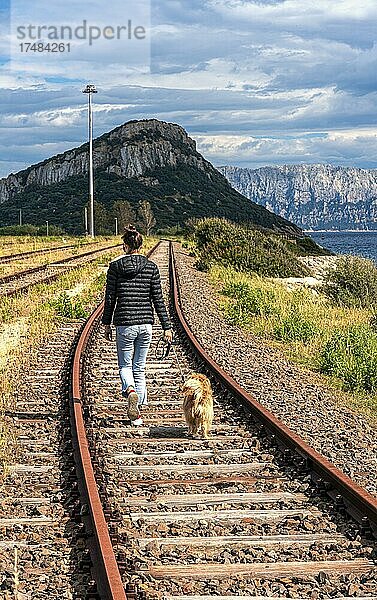 Junge Frau mit Hund spaziert auf dem stillgelegten Gleisbett in der Stadt Figari am Golfo Aranci  Sardinien  Italien  Europa