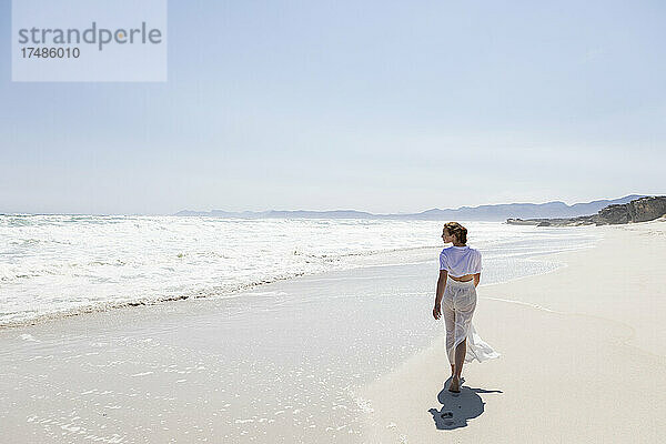 Jugendliches Mädchen  das an einem Sandstrand am Wasser spazieren geht