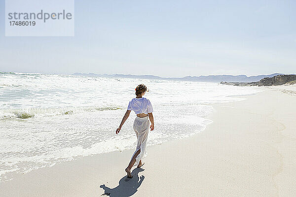 Jugendliches Mädchen  das an einem Sandstrand am Wasser spazieren geht