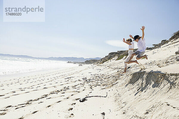 Zwei Kinder  die von einer Sanddüne am Strand springen