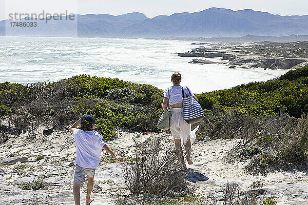 Teenager-Mädchen und jüngerer Bruder mit Blick auf einen Strand und eine felsige Küstenlinie mit Wellen  die an das Ufer schlagen.