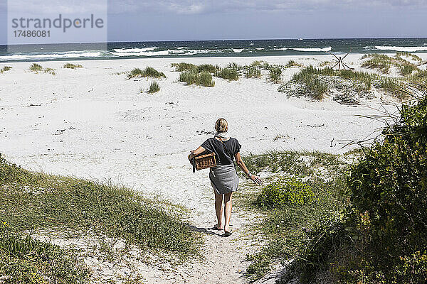 Erwachsene Frau mit Picknickkorb am Grotto Beach  Hermanus  Westkap  Südafrika.