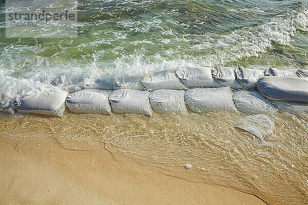 Sandsäcke in Reihen an der Wasserkante  um die Erosion des Strandes zu verhindern