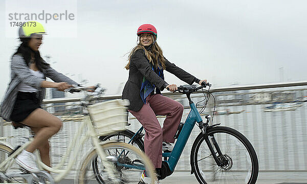 Glückliche junge Frauen Freunde fahren Fahrräder auf städtischen Brücke