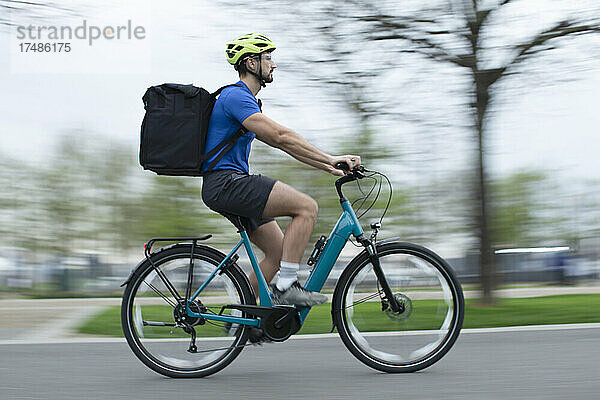 Männlicher Kurier auf dem Fahrrad mit Liefertasche auf dem Bürgersteig