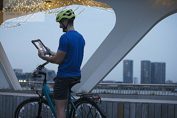 Mann auf dem Fahrrad  Videochat mit digitalem Tablet in der Stadt bei Nacht