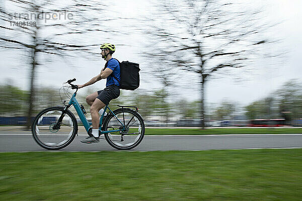 Männlicher Kurier auf dem Fahrrad mit Liefertasche auf einem städtischen Bürgersteig