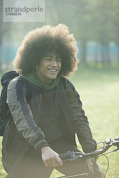 Glücklicher junger Mann mit Afro auf dem Fahrrad im Park