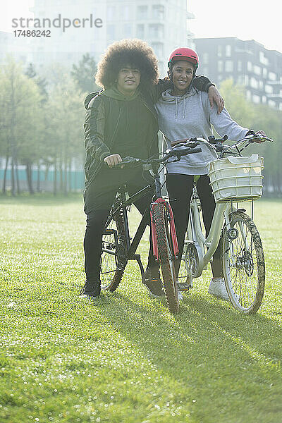 Porträt glückliches Teenager-Paar auf Fahrrädern im städtischen Park Gras
