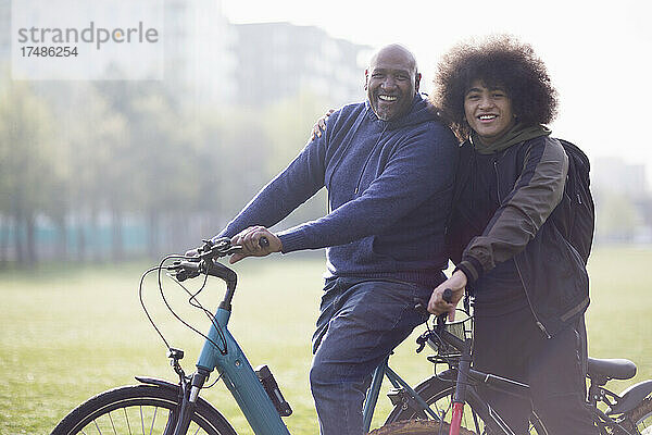 Porträt glücklicher Vater und Teenager-Sohn auf Fahrrädern im Stadtpark