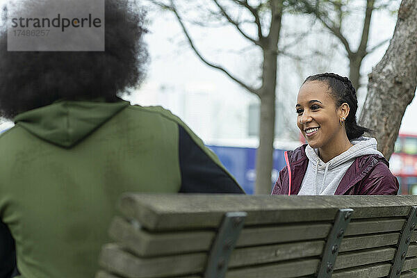 Glückliche junge Frau im Gespräch mit einem Freund auf einer Parkbank