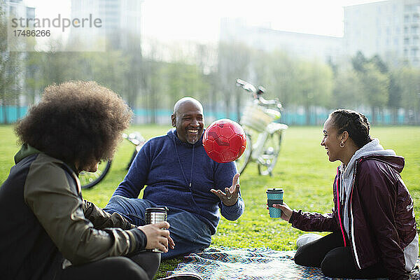 Familie mit Fußball und Kaffee auf der Wiese im Park