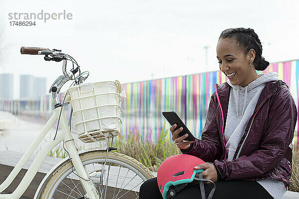 Glückliches Teenager-Mädchen mit Fahrrad und Smartphone