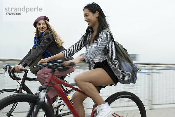 Glückliche junge Frauen  die auf einer Brücke Fahrrad fahren