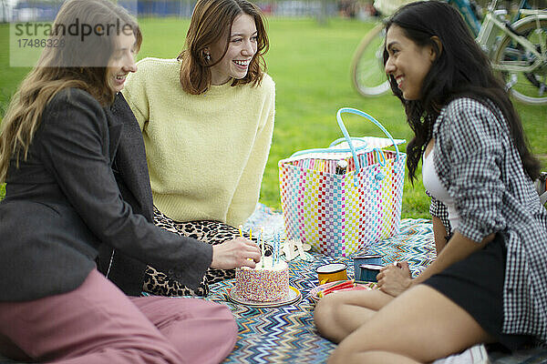 Glückliche junge Frauen Freunde feiern Geburtstag mit Kuchen im Park