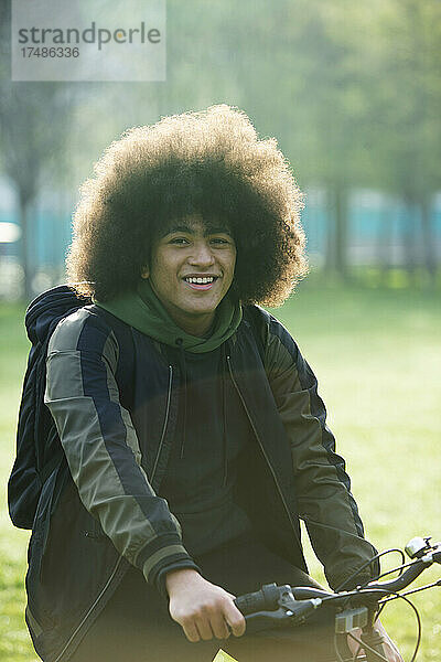 Portrait glücklicher junger Mann mit Afro auf dem Fahrrad im Park