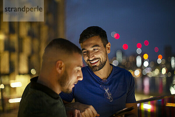 Glückliche Männer mit Smartphone in der Stadt bei Nacht