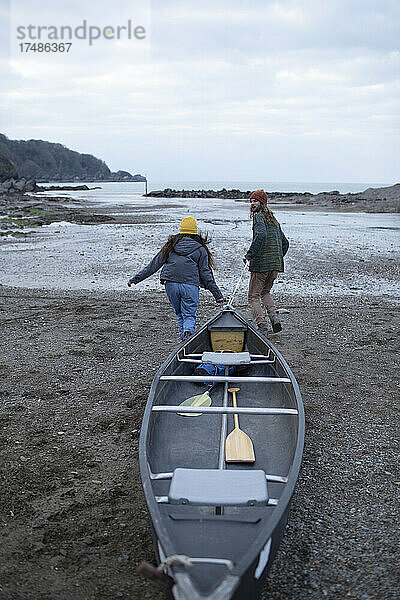 Junges Paar  das ein Kanu am Strand zieht