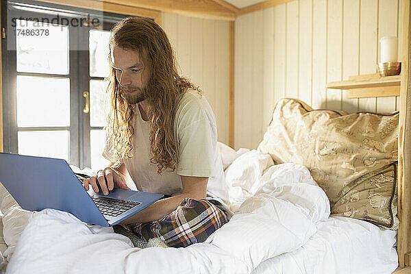 Junger Mann mit Laptop im Bett