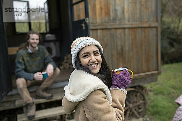 Glückliche junge Frau trinkt Kaffee vor einer kleinen gemieteten Hütte