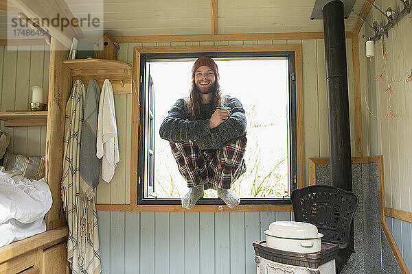 Porträt glücklicher junger Mann im Schlafanzug in winzigem Kabinenfenster