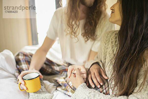 Zärtliches junges Paar mit Kaffee  das sich im Bett an den Händen hält