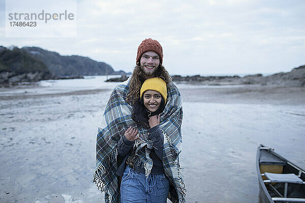 Portrait glückliches junges Paar eingewickelt in eine Decke am Strand