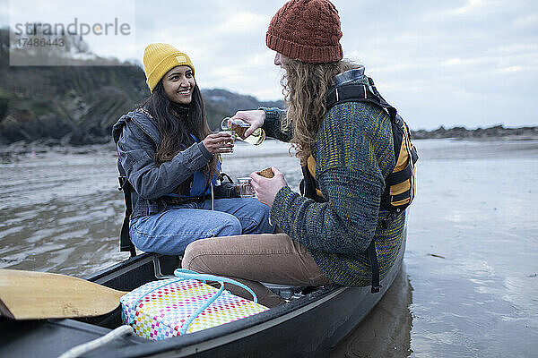 Glückliches junges Paar trinkt Wein in einem Kanu am Strand