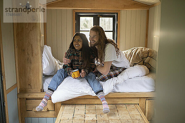 Glückliches junges Paar entspannt sich mit Kaffee in einem winzigen Hüttenmietbett