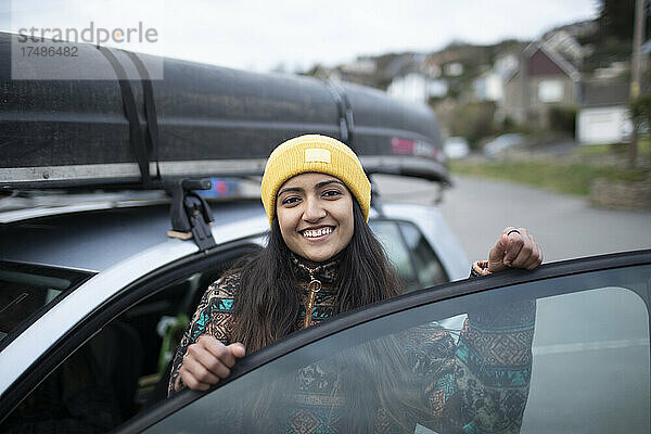 Porträt einer glücklichen jungen Frau  die in ein Auto mit einem Kanu auf dem Dach steigt