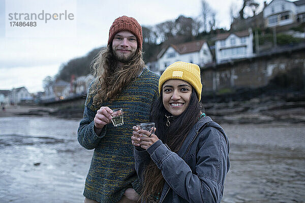Porträt glückliches junges Paar beim Trinken am kalten Strand