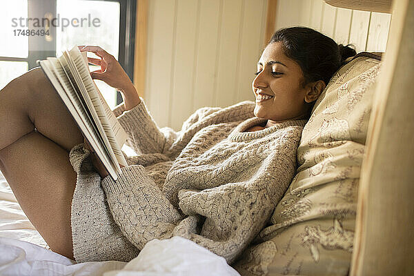 Unbekümmerte junge Frau  die im Bett ein Buch liest