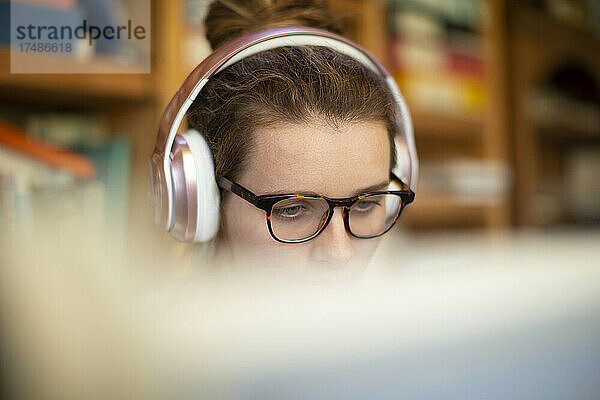 Konzentrierte Frau mit Kopfhörern und Brille  die von zu Hause aus arbeitet