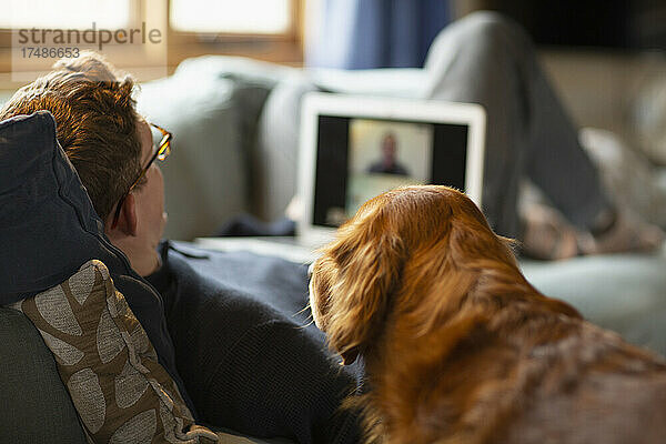 Mann mit Hund beim Videochat mit Laptop auf dem Sofa