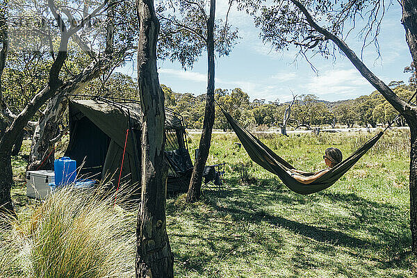 Frau entspannt sich in der Hängematte eines Campingplatzes im sonnigen australischen Busch