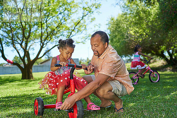 Großvater hilft seiner Enkelin beim Dreiradfahren im Sommerpark