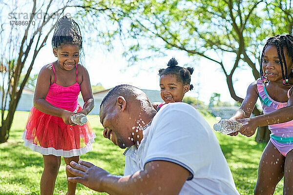 Glückliche verspielte Töchter bespritzen Vater mit Wasserflaschen im Park