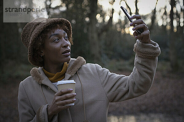 Junge Frau mit Kaffee nimmt Selfie im Herbst Park