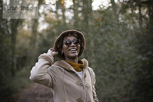 Unbekümmerte junge Frau mit Hut und Sonnenbrille im herbstlichen Park