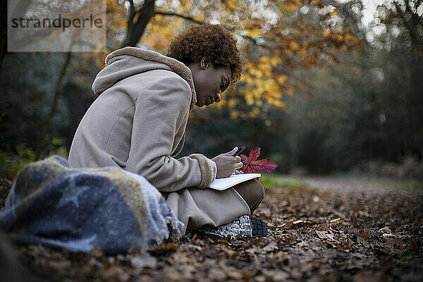 Junge Frau  die in einem ruhigen Herbstpark Tagebuch führt