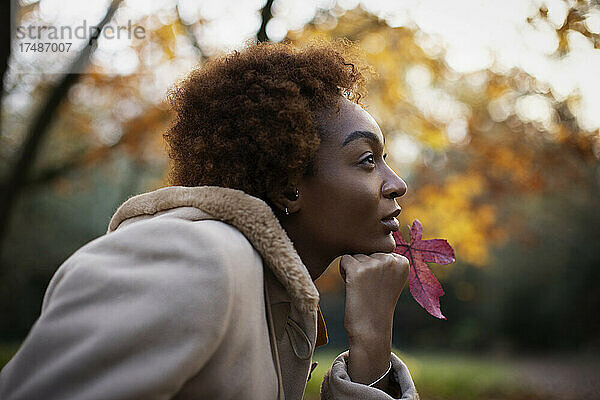 Nachdenkliche junge Frau mit rotem Herbstblatt im Park