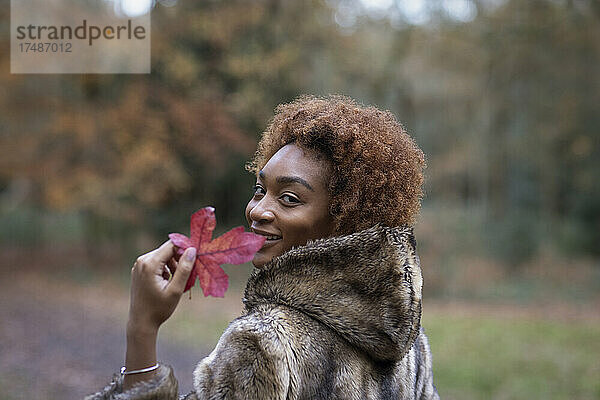 Portrait glückliche junge Frau mit rotem Herbstblatt im Park