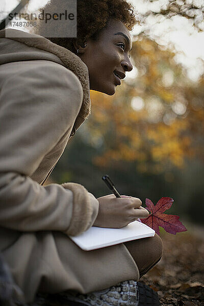 Junge Frau mit Herbstblatt Journaling im Park