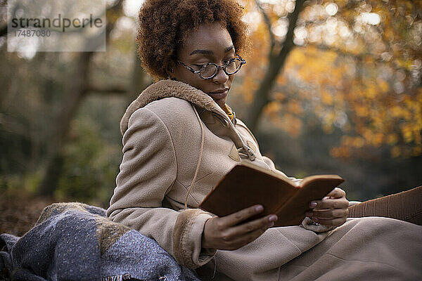 Gelassene junge Frau beim Lesen im herbstlichen Park