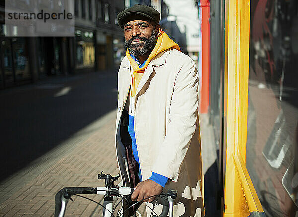 Porträt gut aussehender Mann mit Fahrrad vor einem sonnigen Schaufenster in der Stadt